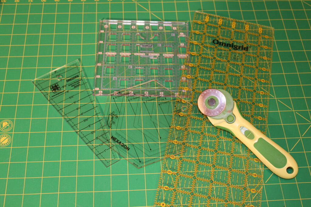 quilting tools for beginners arranged on a cutting mat including rotary cutter ruler and scissors