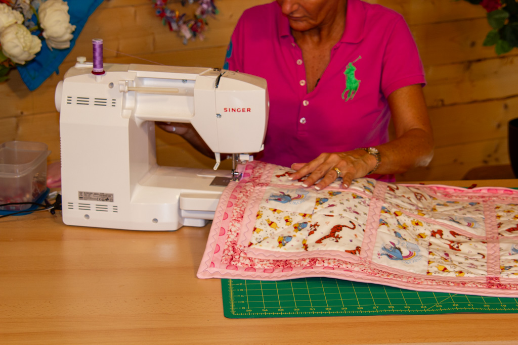 Tracy at her Singer sewing machine stitching pink binding onto a quilt in her studio — how to bind a quilt for beginners