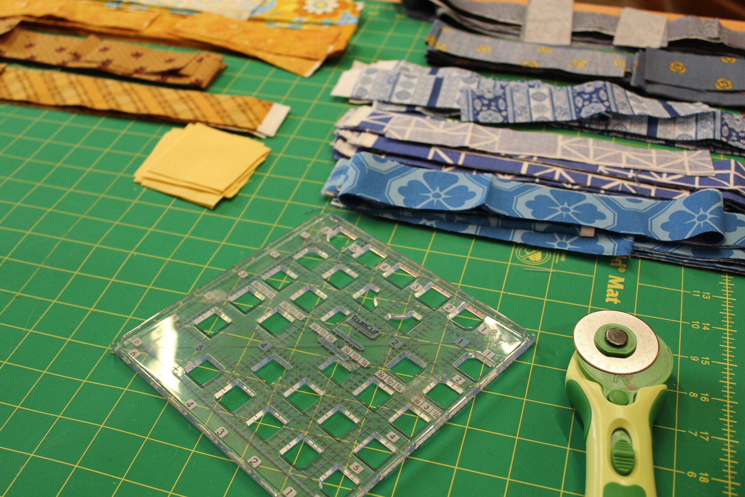 cutting mat with quilting ruler, rotary cutter, and fabric squares — seam allowance in quilting explained