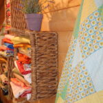 wicker basket of colourful quilting fabrics with finished quilt on wooden floor for beginner quilting