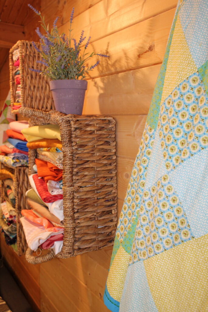 wicker basket of colourful quilting fabrics with finished quilt on wooden floor for beginner quilting